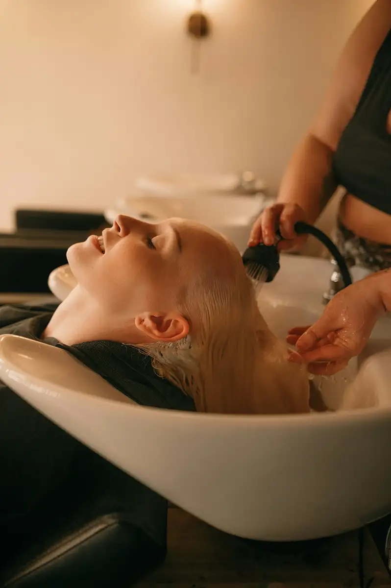 En person som ligger tilbakelent ved en salongvask mens en stylist vasker håret med en håndholdt dusjmunnstykke.